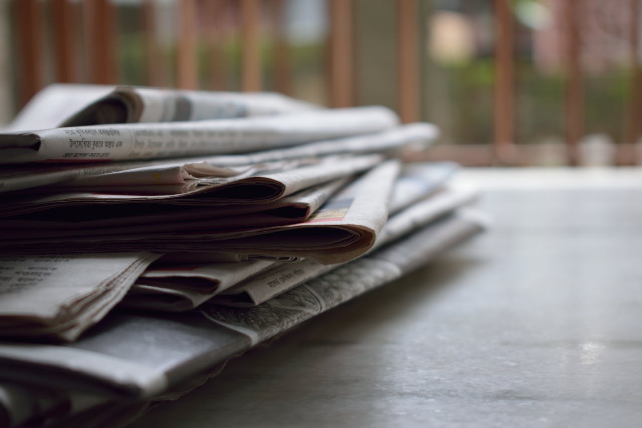 team-03 A close-up of a stack of newspapers resting on a desk, symbolizing information and media.